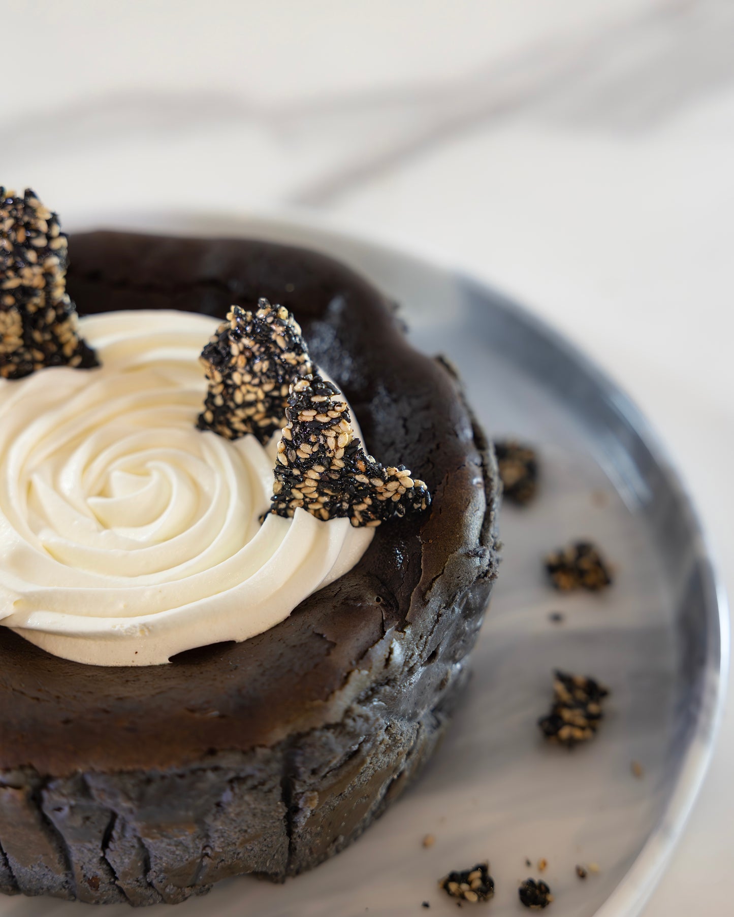 A slice of Kuki black sesame Basque burnt cheesecake with a swirl of white cream on top, garnished with Kuki sesame brittles around the plate.
Okaeri Bakery - London based Asian Bakery