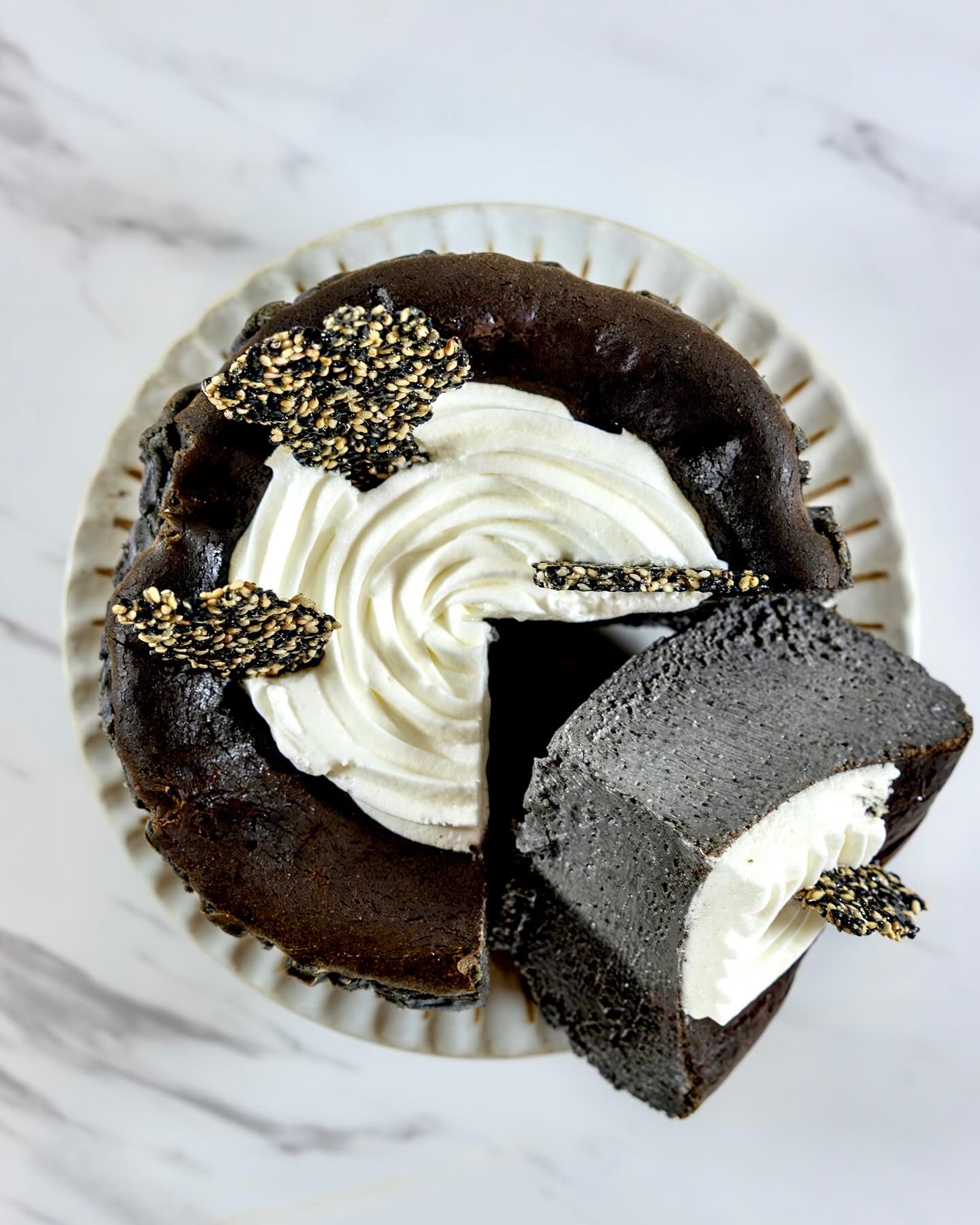 A slice of Kuki black sesame Basque burnt cheesecake with a swirl of white cream on top, garnished with Kuki sesame brittles.
Okaeri Bakery - London based Asian Bakery