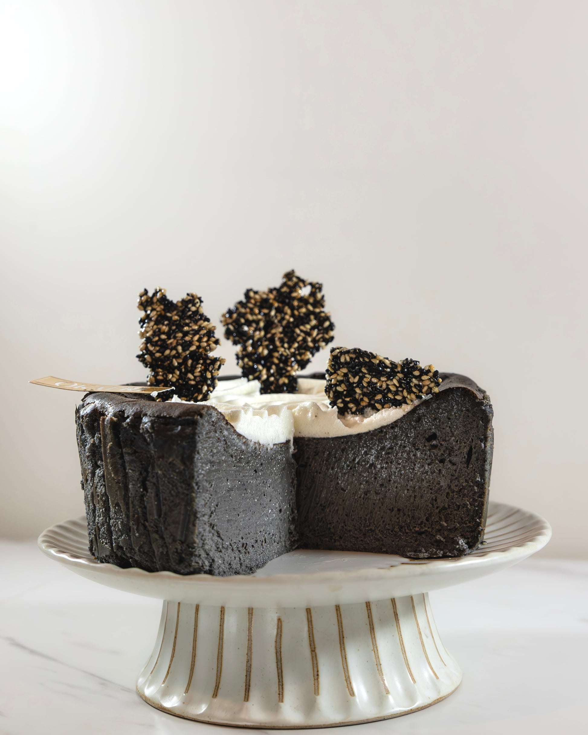 A slice of Kuki black sesame Basque burnt cheesecake with a swirl of white cream on top, garnished with Kuki sesame brittles.
Okaeri Bakery - London based Asian Bakery